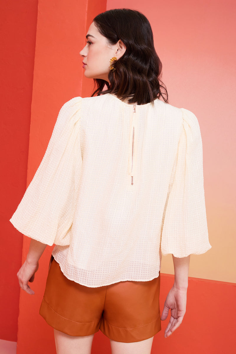 off-white top with full paper bag sleeves and a zipper at the back of the neckline