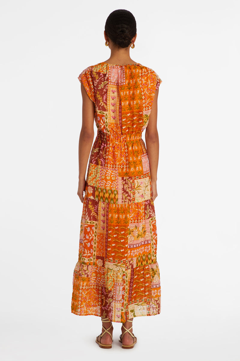 An orange floral patchwork printed maxi dress with a v-neckline and a thick waistband that can be adjusted using a tie